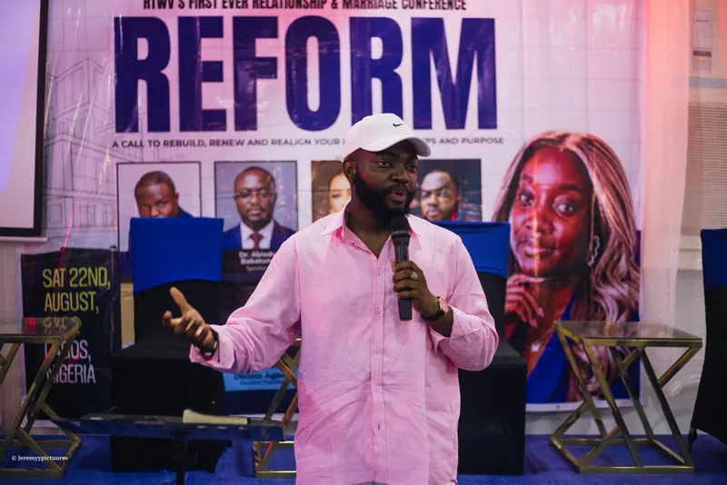 A speaker in a pink shirt and white cap addressing the room at the Reform conference